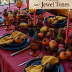 Thanksgiving fruit and foliage tablescape with cranberry linens and jewel tone table