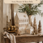 Neutral holiday village with evergreen branches and a linen bow beneath a banner reading A Little Christmas Village Ivory Houses and Brass Bells