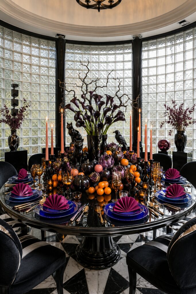 Halloween table in a glass block rotunda with black calla lilies citrus black pumpkins cobalt plates plum fan napkins and amber goblets