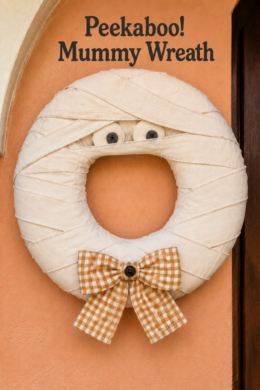 Peekaboo Mummy Wreath text above a Halloween ring wrapped in overlapping ivory strips with soft eyes and a golden checked bow