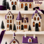 Purple roof Halloween village displayed on ivory shelves with velvet ribbon and miniature black trees