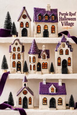 Purple roof Halloween village displayed on ivory shelves with velvet ribbon and miniature black trees