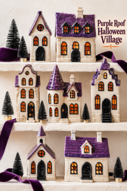 Purple roof Halloween village displayed on ivory shelves with velvet ribbon and miniature black trees