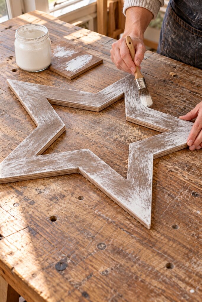 Hand dry brushing white streaks onto a brown plywood star frame beside a painted test scrap