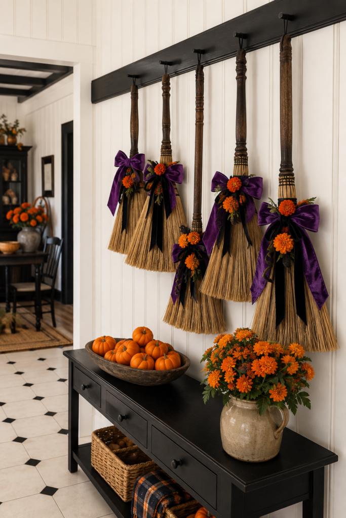 Halloween broom wall with five hanging straw brooms purple bows orange flowers and mini pumpkins on an entry console