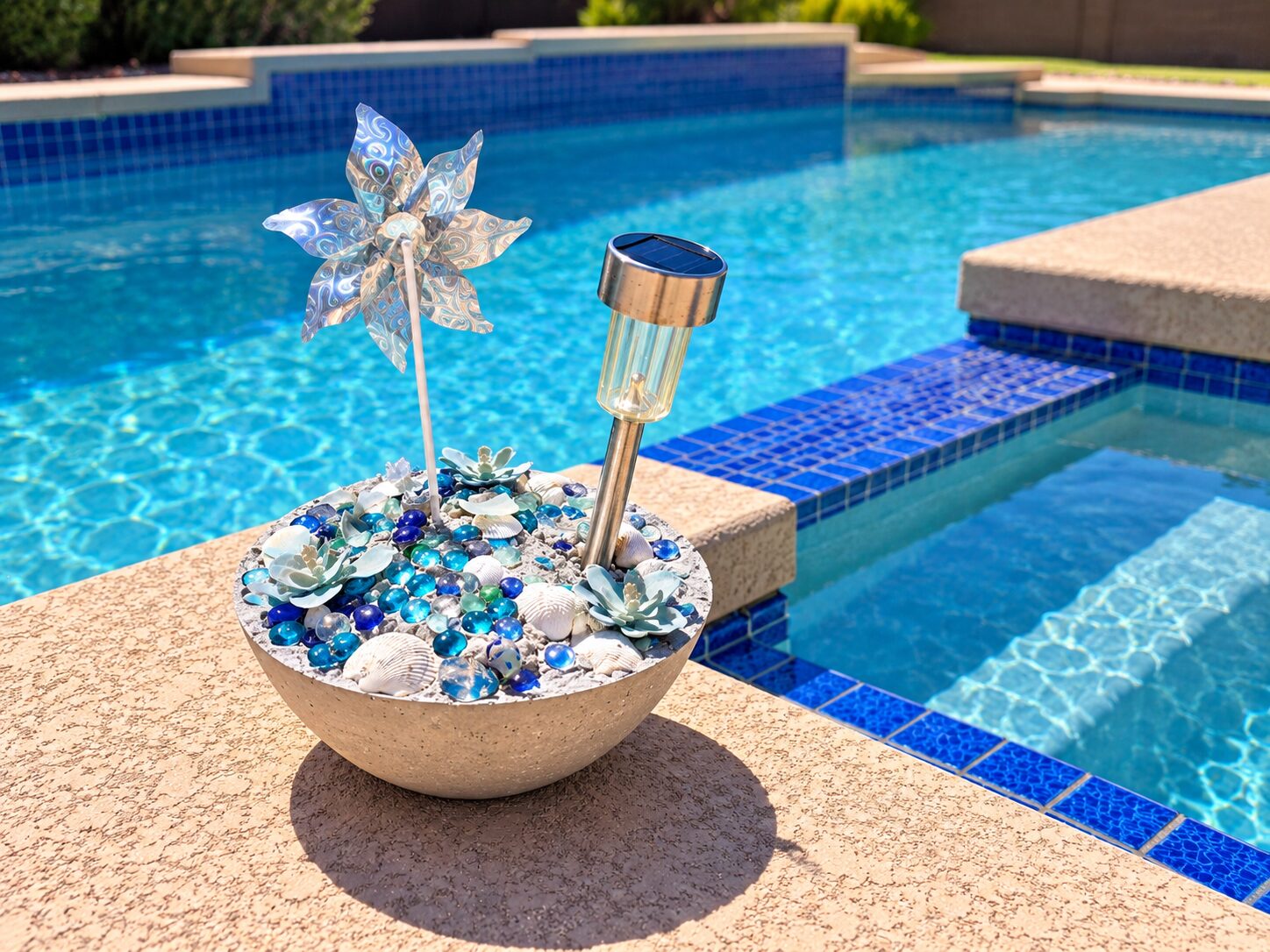 concrete bowl with marbles and cacti holding a pinwheel by swimming pool edge