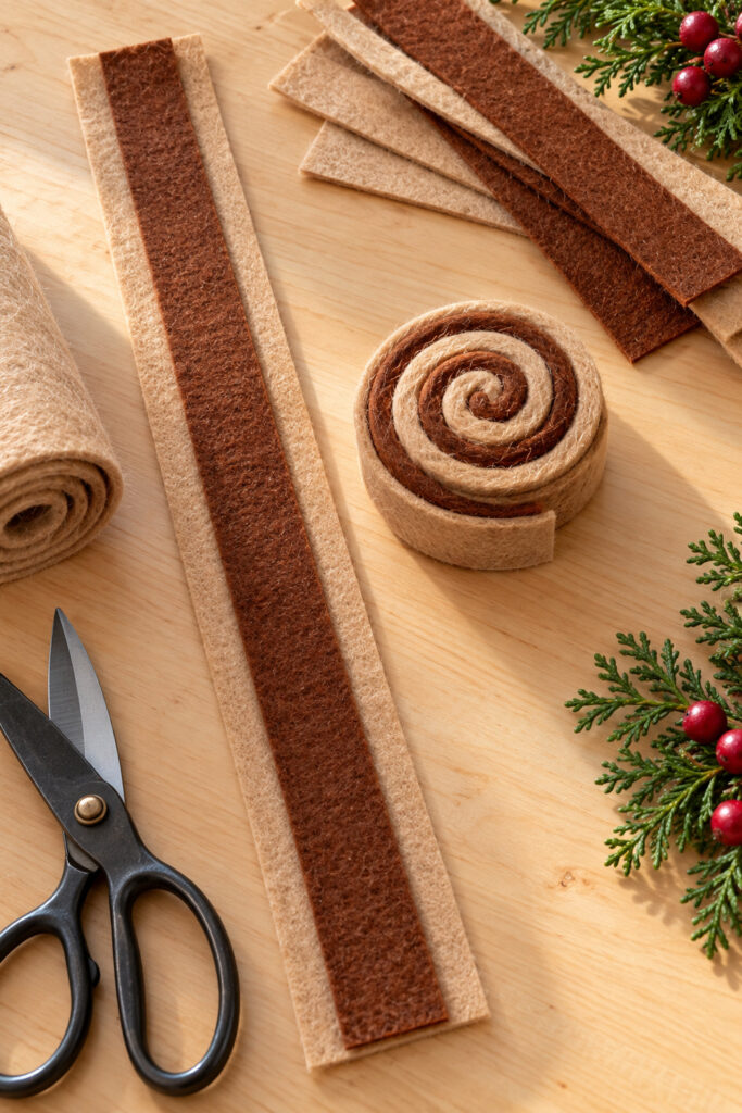 Brown felt centered on a tan strip beside an uniced spiral cinnamon roll on a wooden worktable