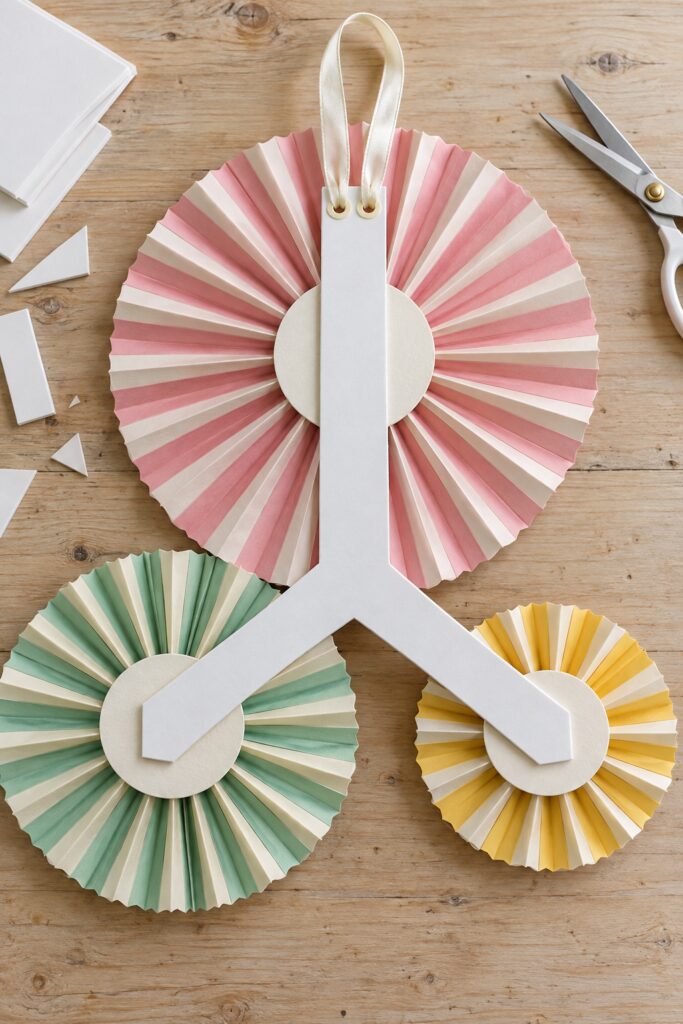 Rear view of three pastel paper fans connected at their reinforced centers by one foam board backing with a ribbon hanging loop