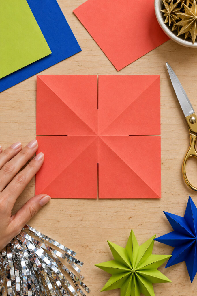 Coral paper square with diagonal and center creases and four slits stopping halfway toward the center