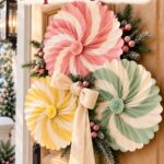 Pastel pleated paper Christmas door decoration with a cream bow beneath the words Make These Paper Rosettes